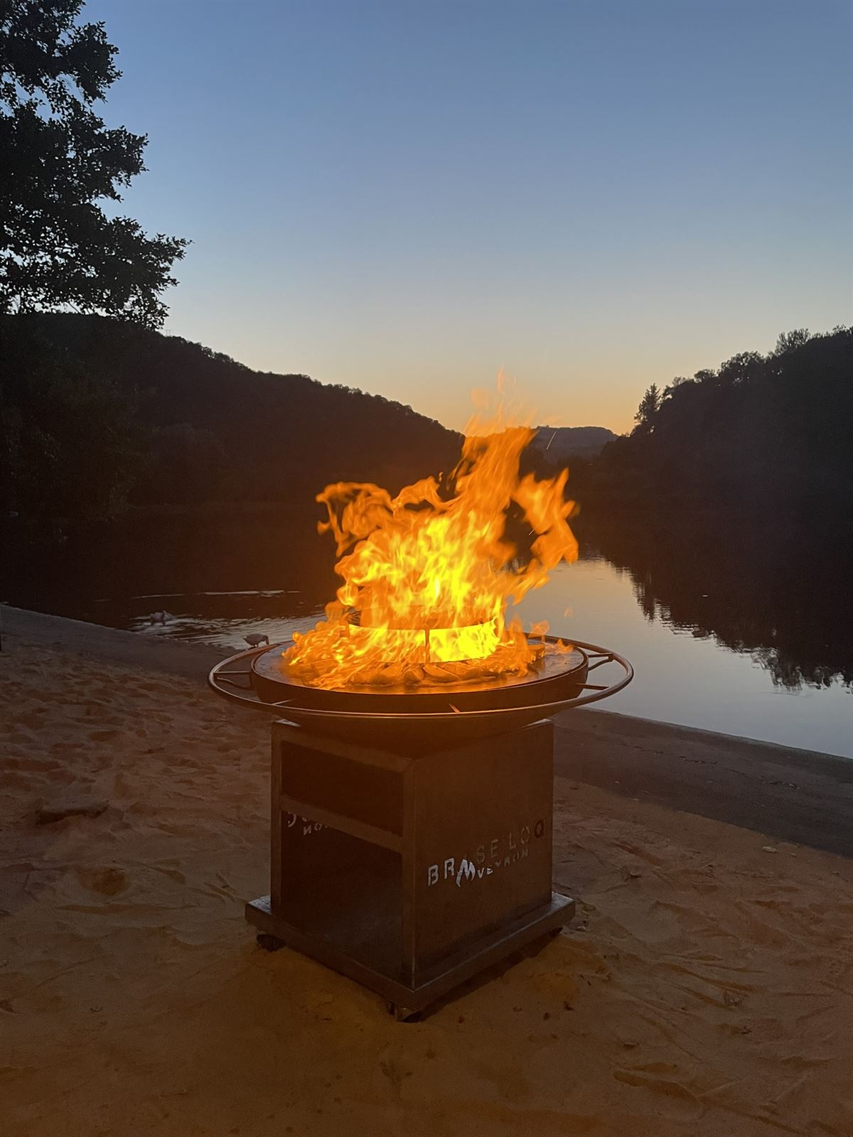 Brasero avec de grandes flammes au bord d'une rivière au crépuscule