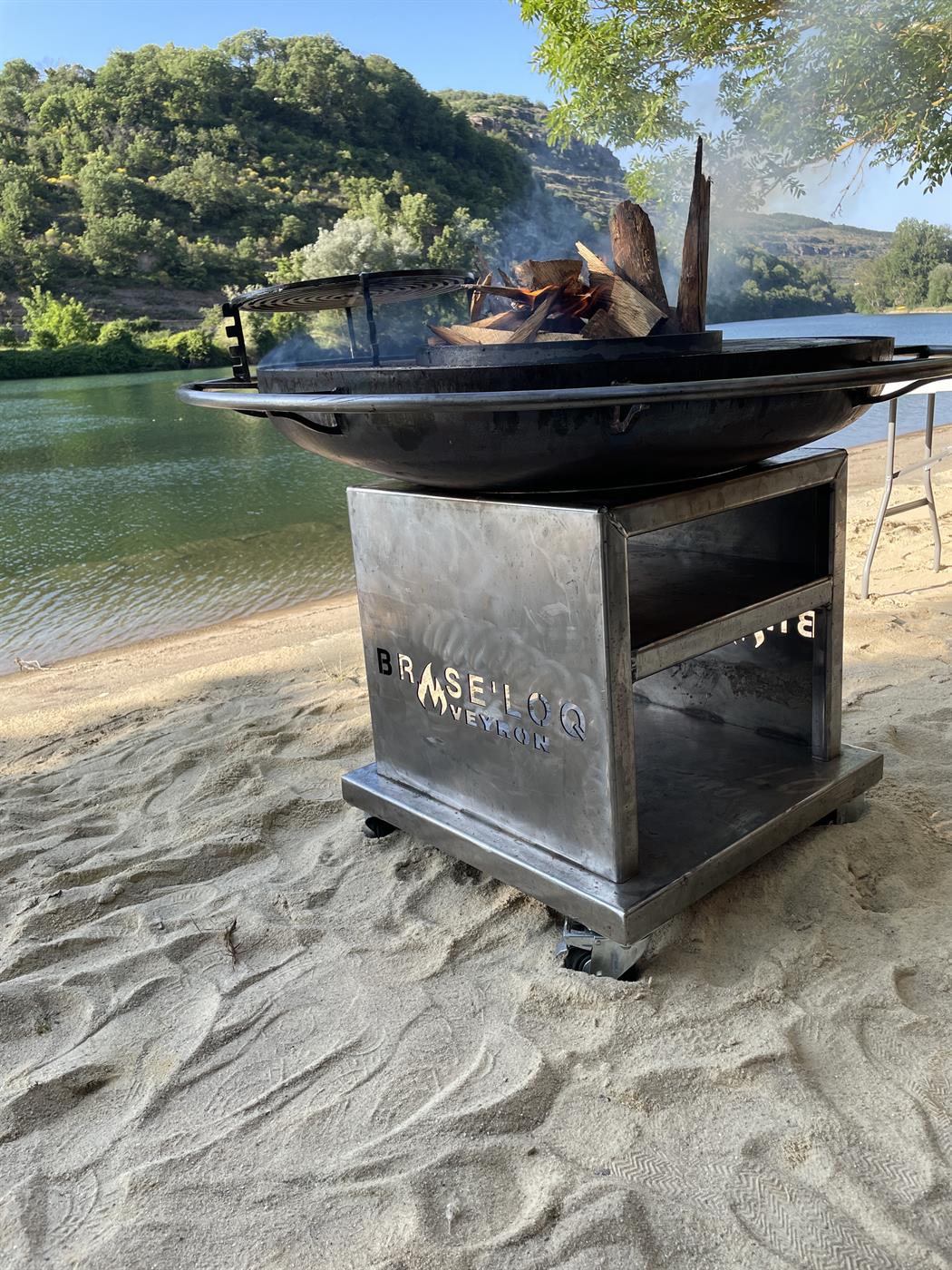 Brasero allumé sur une plage de sable au bord d'une rivière, ciel bleu nuit